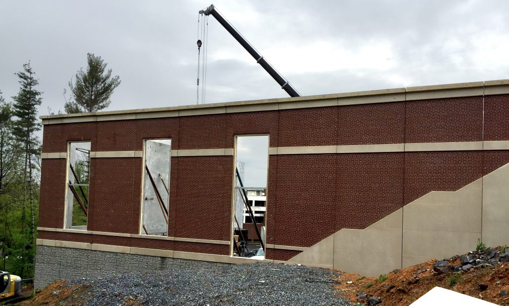 A building under construction. A crane can be seen in the background lifting precast concrete wall panels into place.